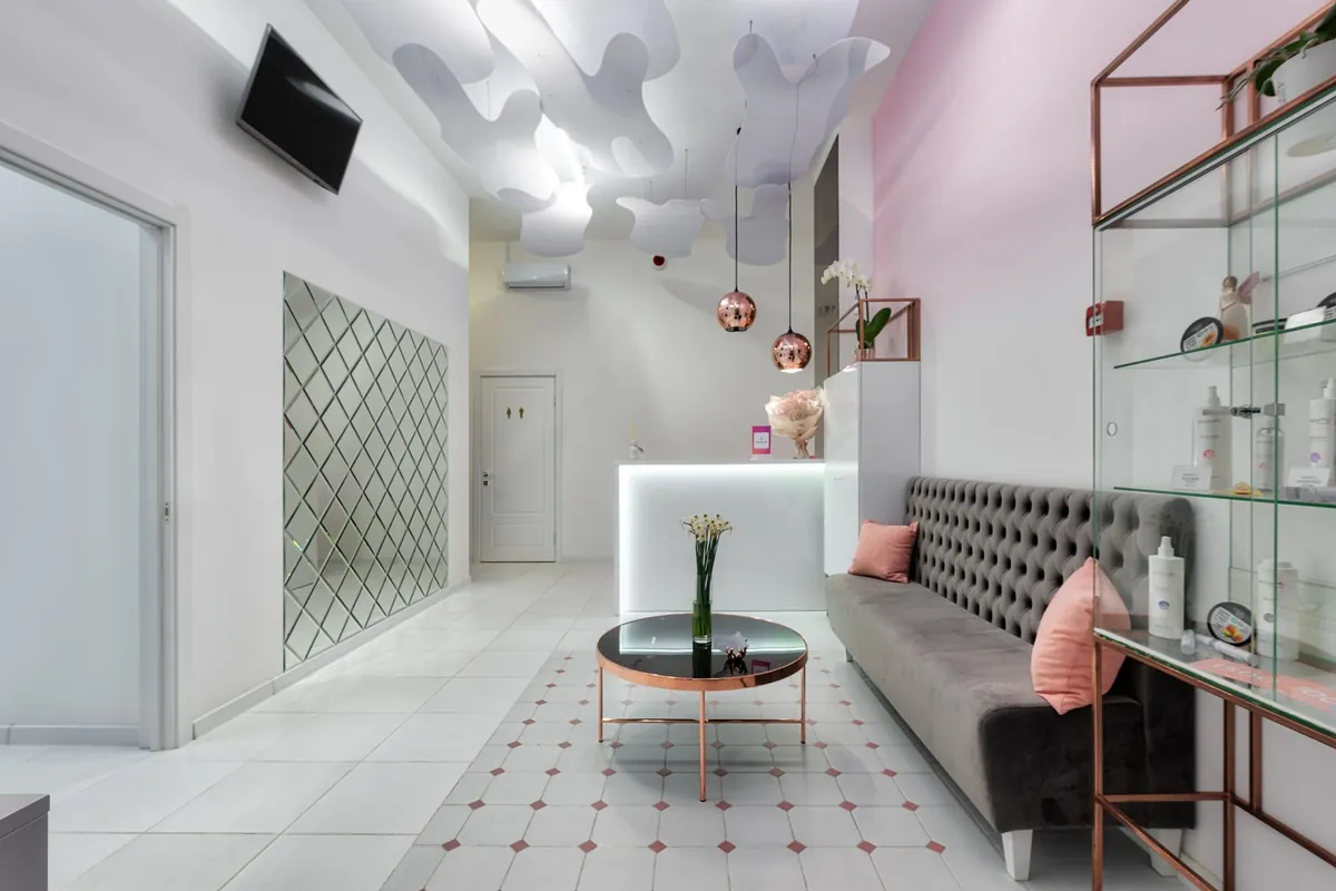 An elegant clinic reception lounge with a tufted sofa, a glass table with white flowers and soft pink walls