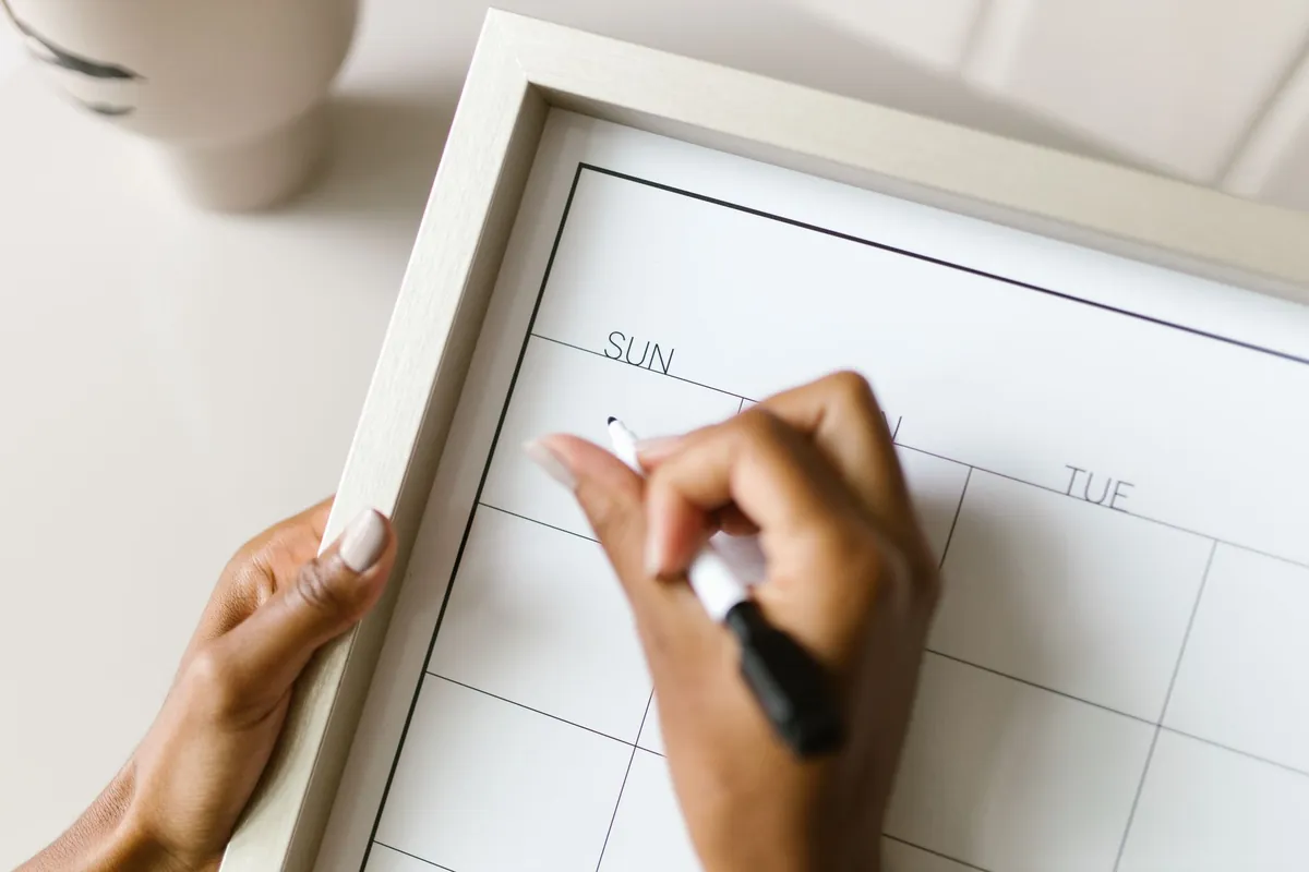 Hands writing on a weekly wall calendar, planning which days are open