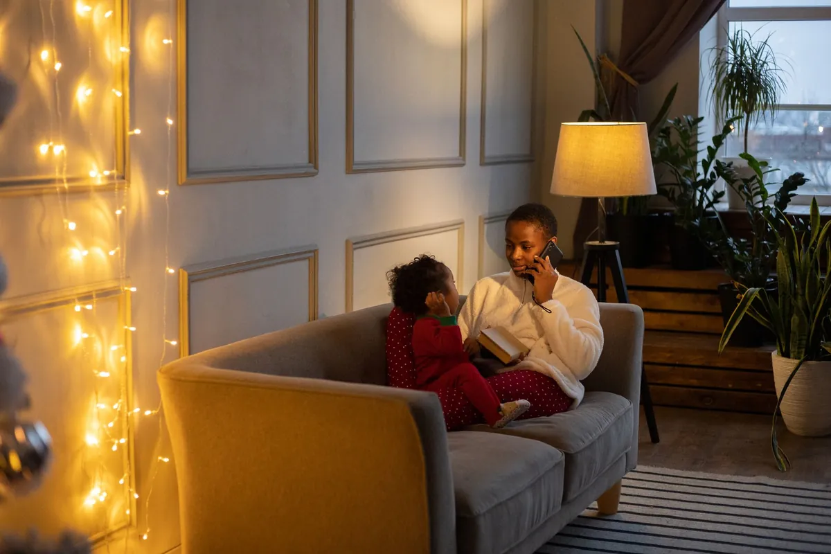 A parent on the phone in the evening, sitting on a sofa with a young child in pyjamas